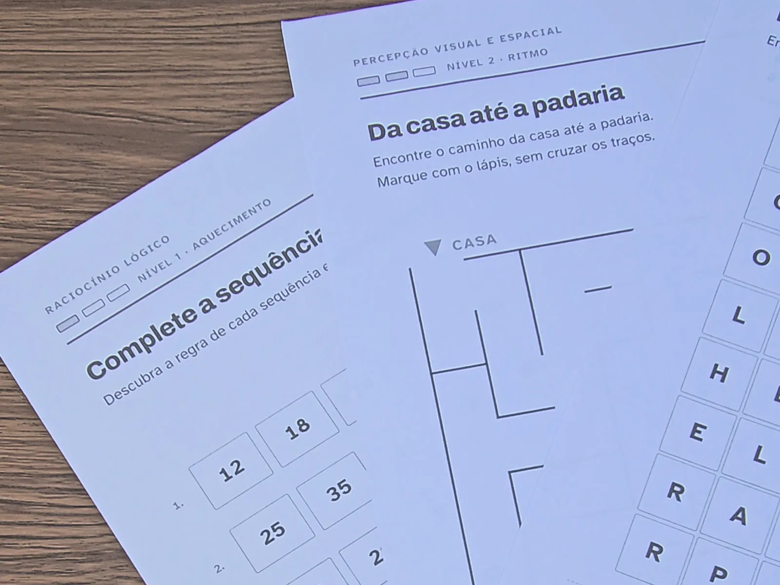 Folhas do kit sobrepostas sobre a mesa: sequências numéricas, labirinto e caça-palavras